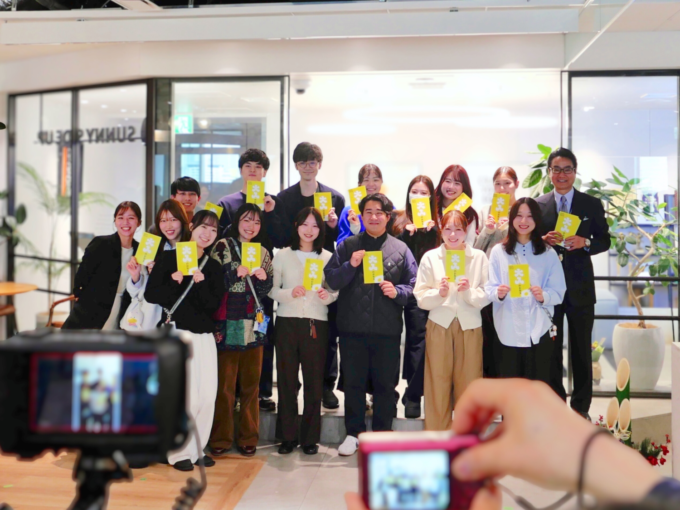 「大人のお年玉」ポチ袋を持った、サニーサイドアップグループ副社長 渡邊と新卒メンバーのし集合写真